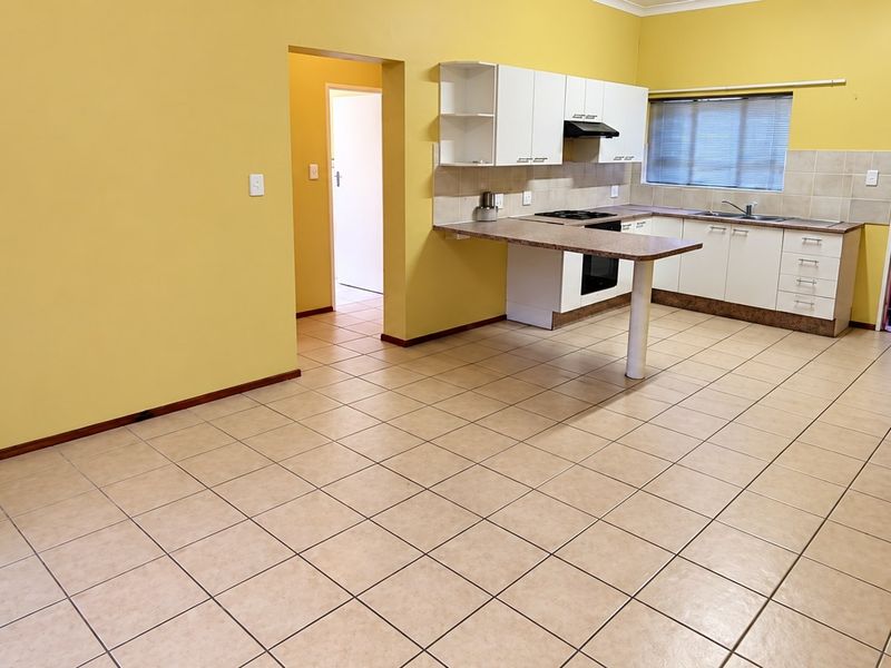 Spacious open-plan kitchen and living area featuring tiled flooring, white cabinetry, a breakfast bar, and direct access to an exterior entrance.
