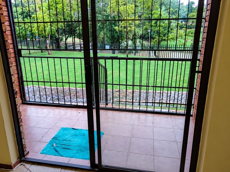 A covered patio area featuring tiled flooring, a sliding glass door with security gate, and direct access to a private garden space.
