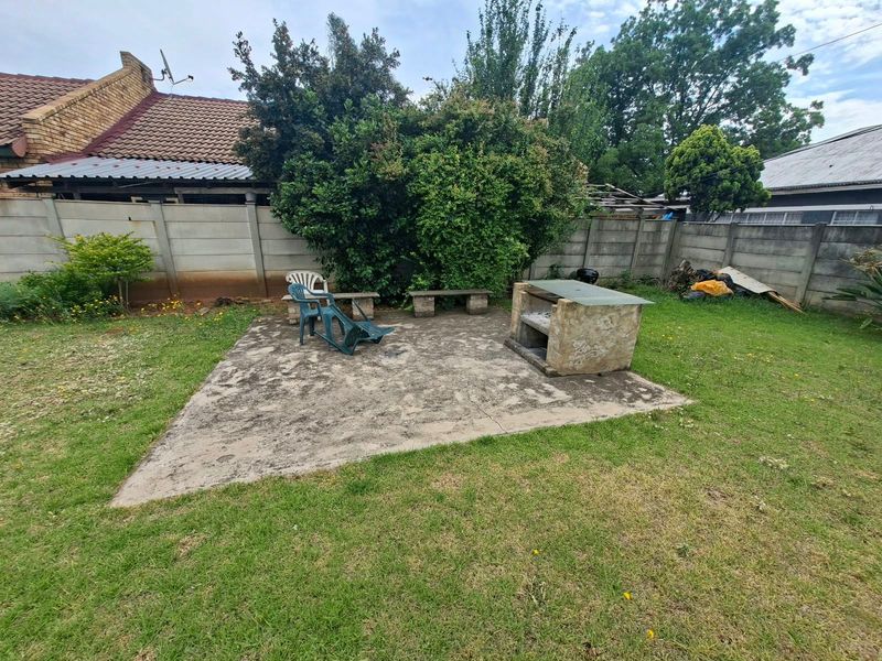 Rear garden area featuring a concrete patio, built-in braai, and precast boundary walling, offering potential for outdoor entertainment space development.