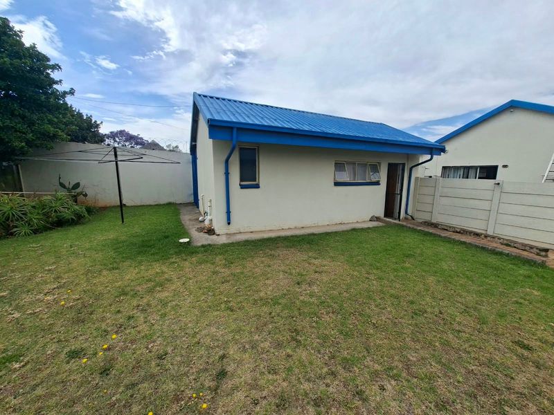 Rear view of the apartment building featuring a blue corrugated metal roof, white exterior walls, and a private garden area with boundary walling.