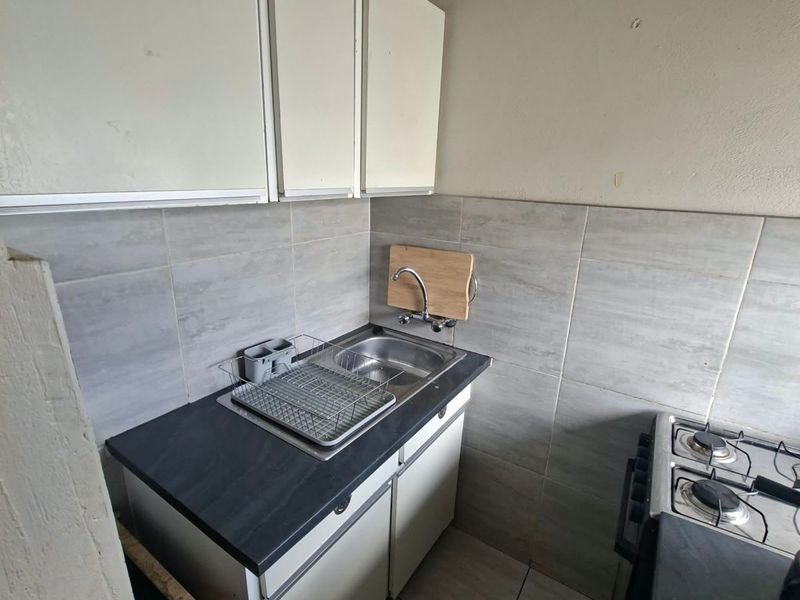 Compact kitchen area featuring built-in cabinetry, a stainless steel sink, tiled backsplash, and a gas hob with tiled flooring.