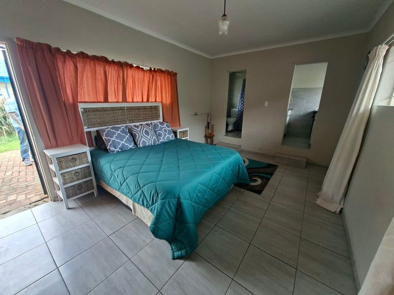 A bedroom featuring tiled flooring, direct access to an outdoor patio, and an en-suite bathroom entrance.