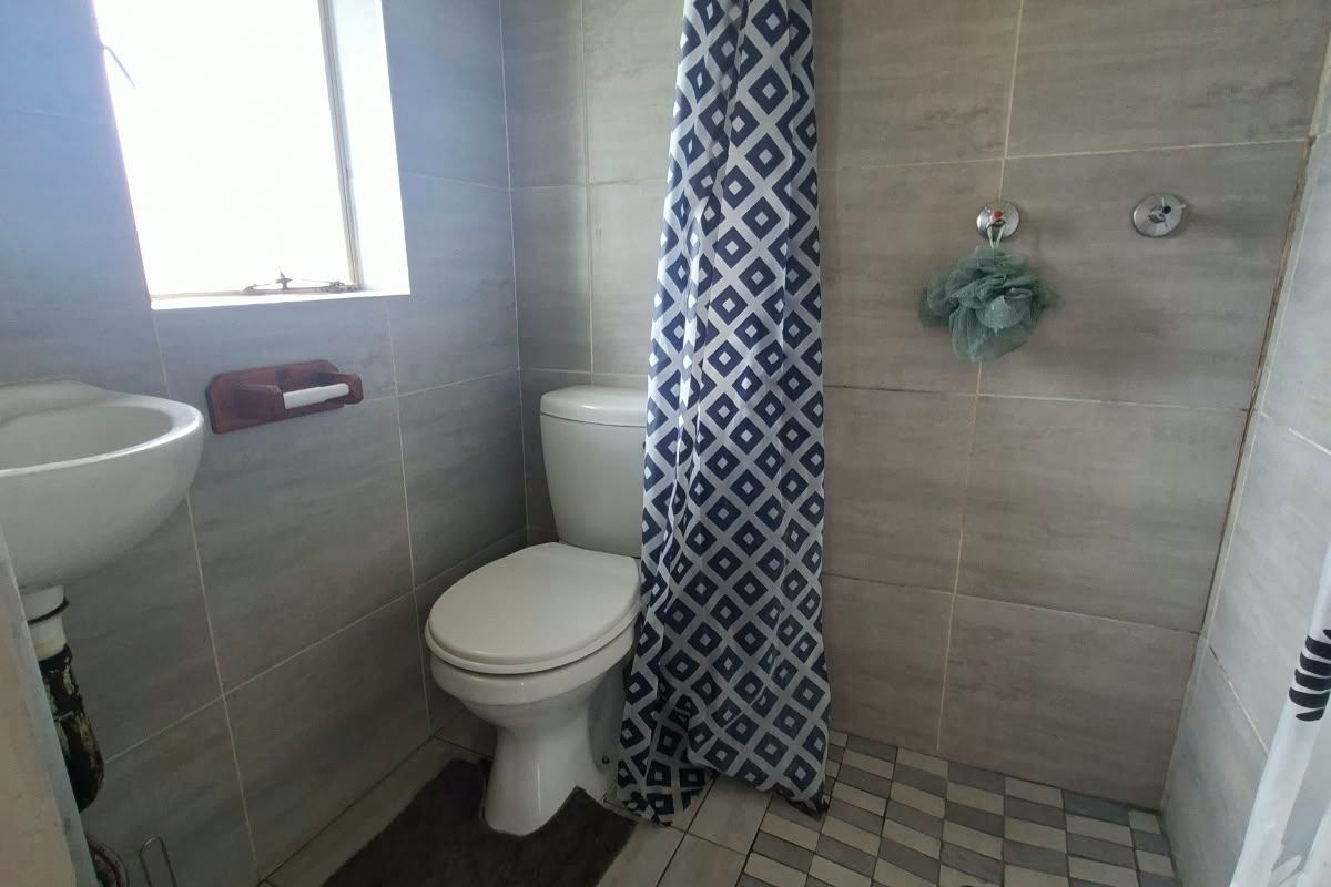 A compact bathroom featuring tiled walls and flooring, a wall-mounted basin, a toilet, and a shower area with a fixed shower head.