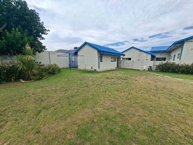 A spacious rear garden area featuring a lawn, perimeter precast concrete walling, and a detached outbuilding with a blue metal roof.