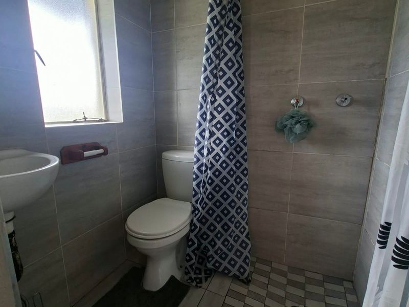 Compact bathroom featuring tiled walls and flooring, a wall-mounted basin, and a shower area with a fixed shower head.