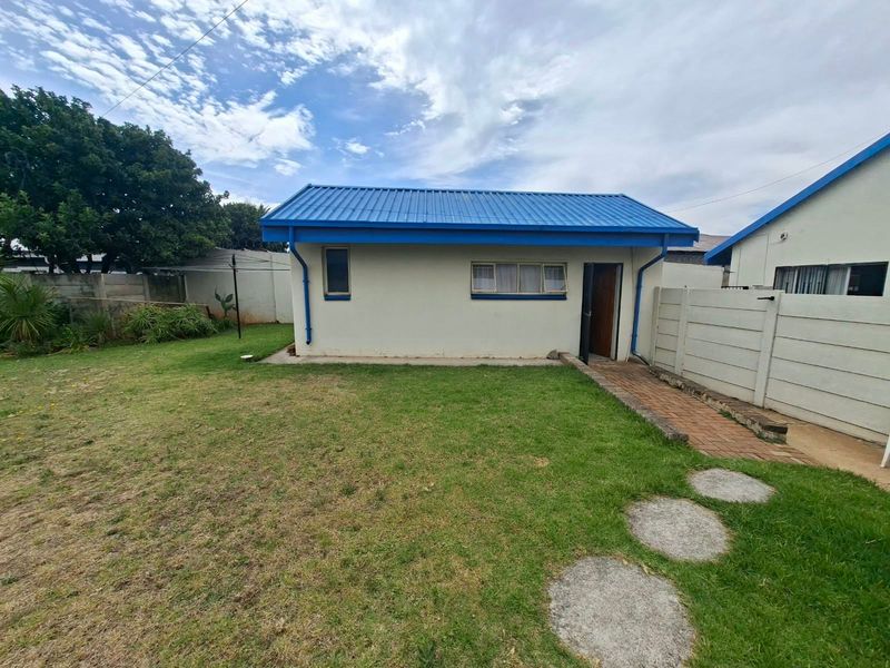 Rear view of the property featuring a blue corrugated metal roof, paved walkway, and a private garden area enclosed by precast concrete walls.