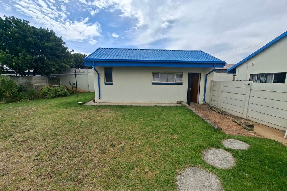 Rear view of the property featuring a blue corrugated metal roof, paved walkway, and a private garden area enclosed by precast concrete walls.
