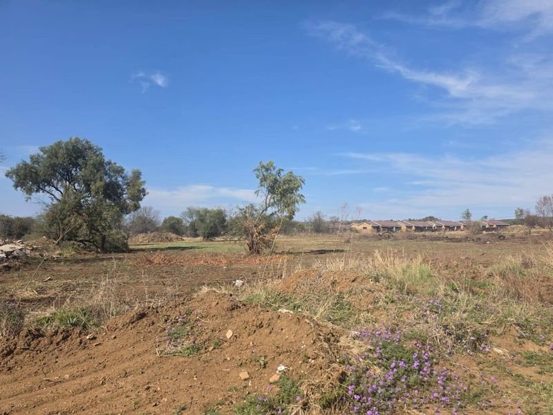 A view of a vacant residential plot featuring natural vegetation, trees, and open land, suitable for future development.