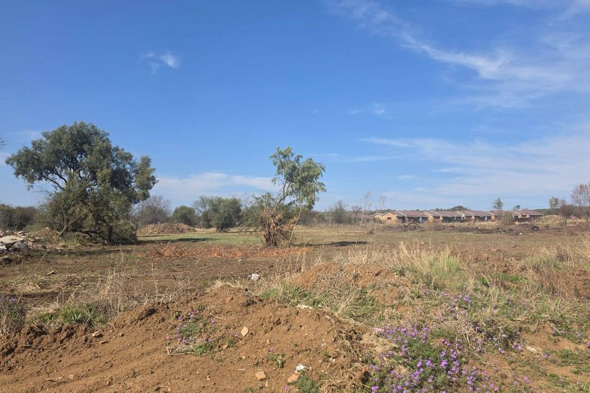 A view of a vacant residential plot featuring natural vegetation, trees, and open land, suitable for future development.