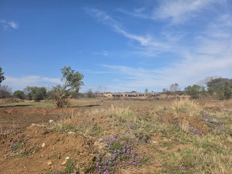 A view of an undeveloped residential plot of land with natural vegetation and distant neighboring properties.