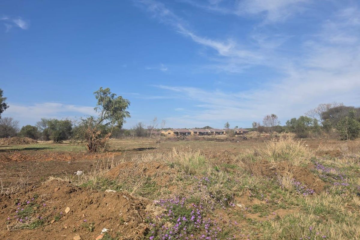 A view of an undeveloped residential plot of land with natural vegetation and distant neighboring properties.