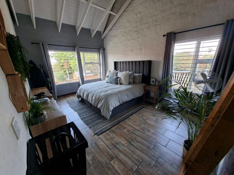 Spacious bedroom featuring a high vaulted ceiling with exposed rafters, tiled flooring, and large windows with security bars.