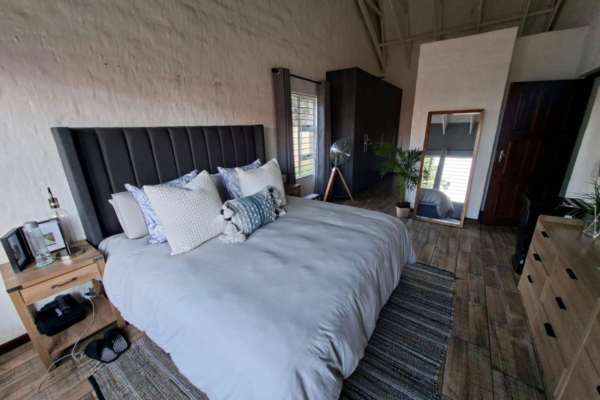 Spacious bedroom featuring high vaulted ceilings with exposed rafters, textured masonry walls, tiled flooring, and a large built-in wardrobe.