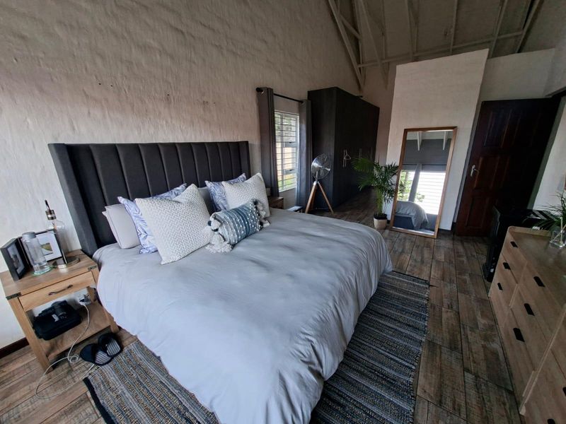 Spacious bedroom featuring high vaulted ceilings with exposed rafters, textured masonry walls, tiled flooring, and a large built-in wardrobe.