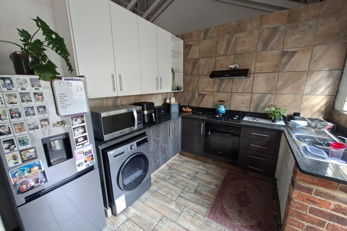 Functional kitchen featuring dark wood lower cabinetry, white upper cabinets, granite countertops, built-in oven, gas hob, and tiled finishes throughout.