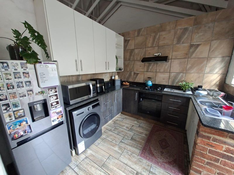 Functional kitchen featuring dark wood lower cabinetry, white upper cabinets, granite countertops, built-in oven, gas hob, and tiled finishes throughout.