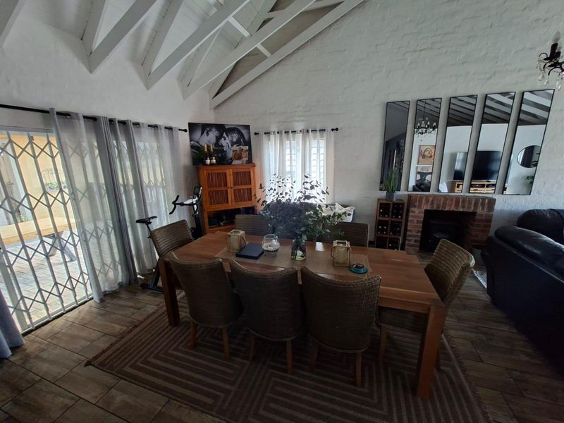 Spacious dining area featuring a vaulted ceiling with exposed rafters, a brick fireplace, and direct access to the patio through a security gate.