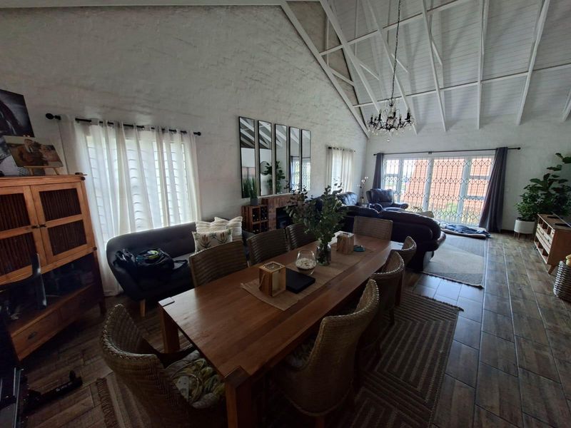 Spacious open-plan living and dining area featuring a high vaulted ceiling with exposed trusses, tiled flooring, and a fireplace.