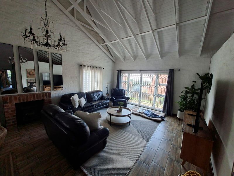 Spacious living room featuring a high vaulted ceiling with exposed timber trusses, a brick fireplace, and tiled flooring with access to the exterior.