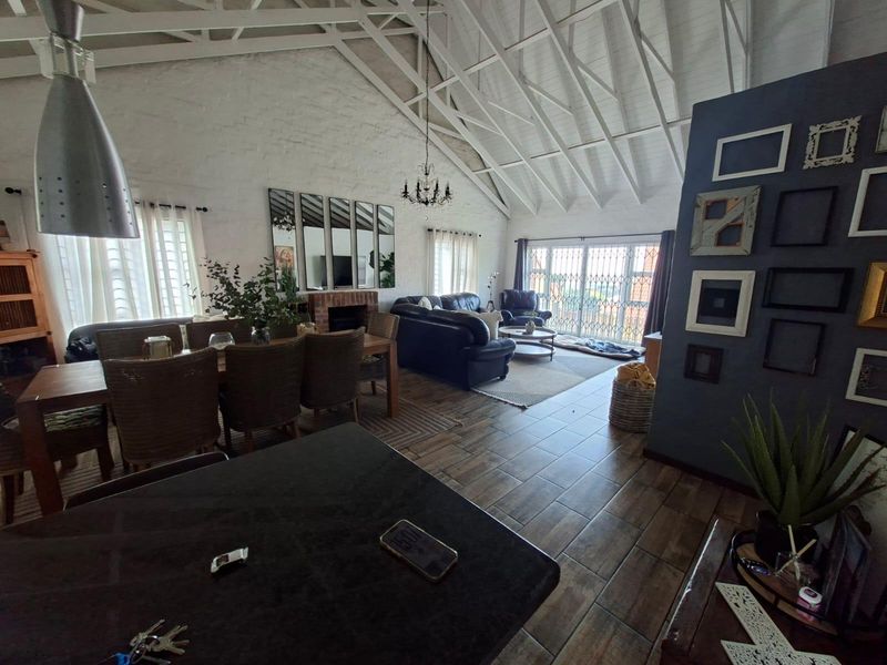 Spacious open-plan living and dining area featuring a high vaulted ceiling with exposed trusses, tiled flooring, and a brick fireplace.