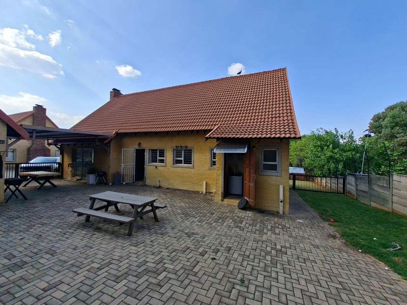 Rear view of the house featuring a large paved patio area, covered outdoor space, and traditional terracotta roof tiles.