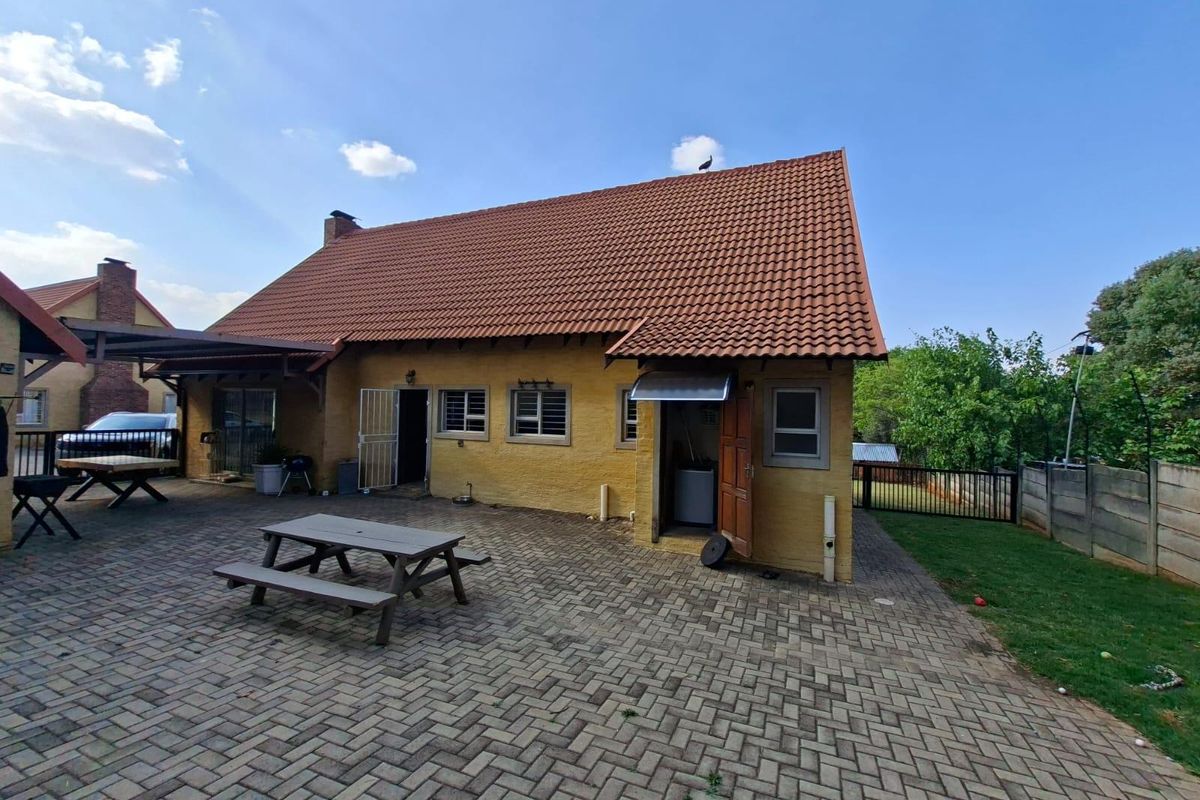 Rear view of the house featuring a large paved patio area, covered outdoor space, and traditional terracotta roof tiles.