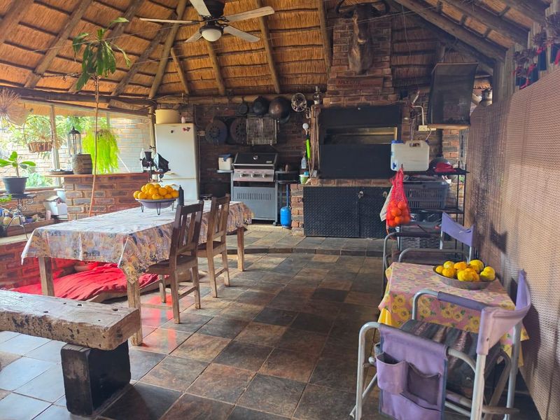 A spacious covered patio featuring a traditional thatched roof, exposed brickwork, and a built-in braai area, ideal for outdoor entertaining.