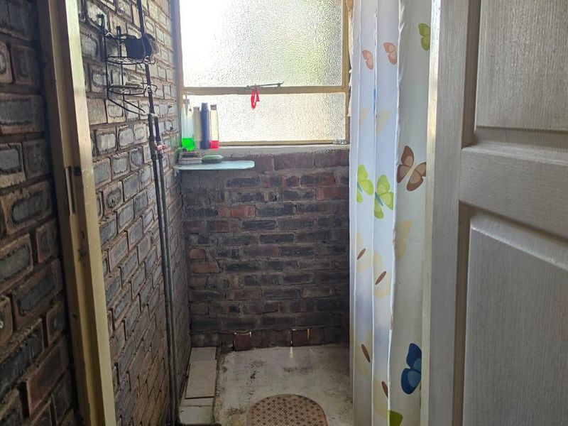 A rustic bathroom featuring exposed brick walls, a shower area with exposed plumbing, and an obscured glass window.