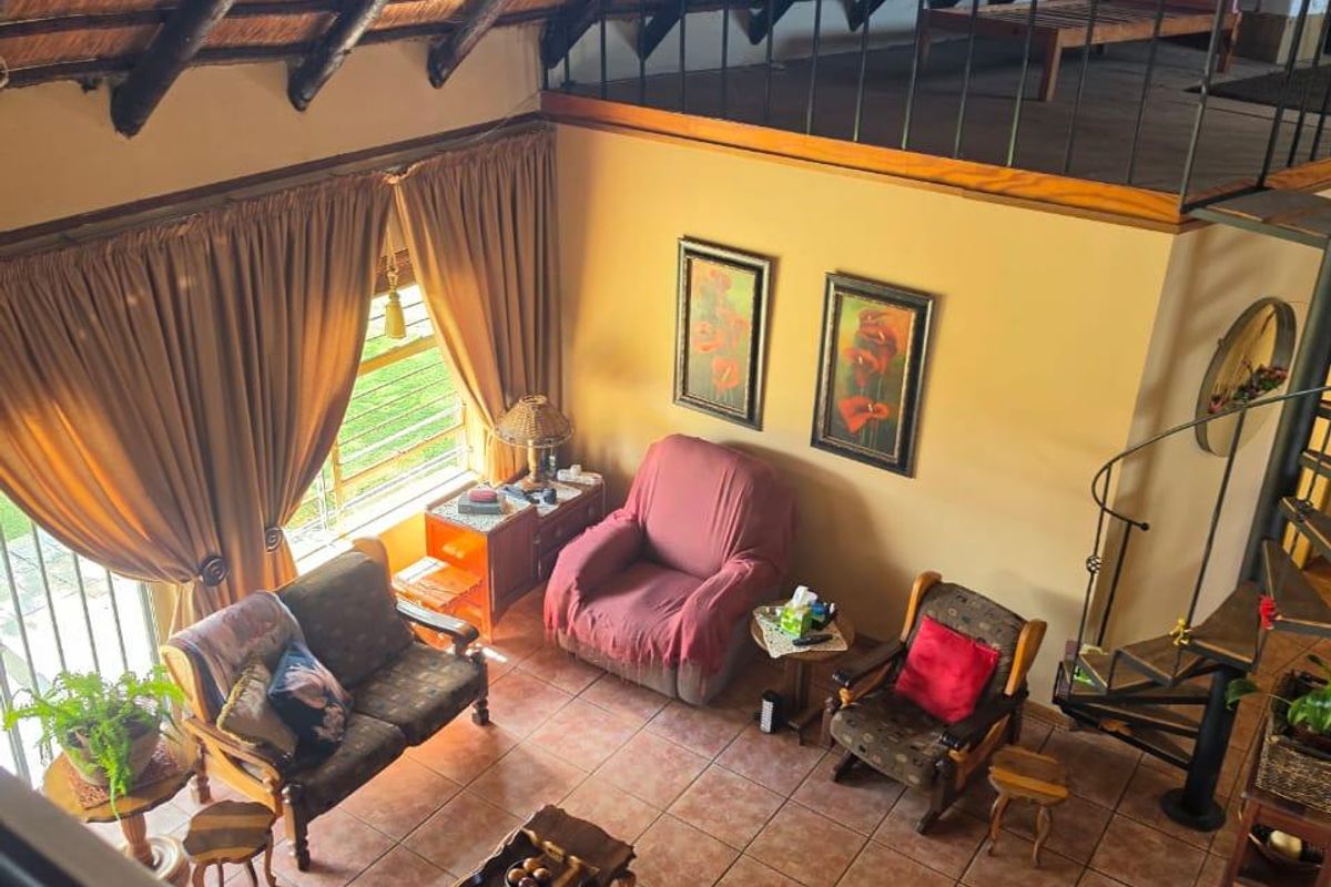Spacious double-volume living area featuring a traditional thatched roof with exposed timber rafters, a mezzanine level, and a spiral staircase.