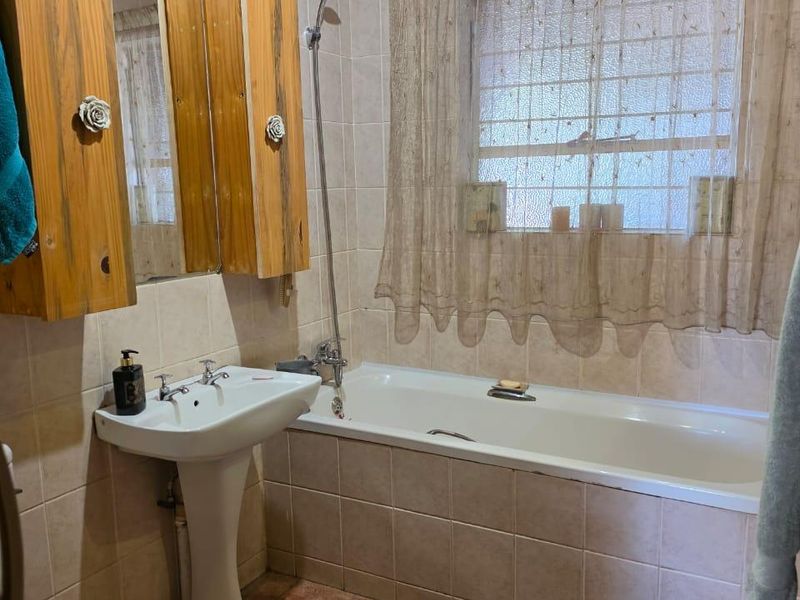 A functional bathroom featuring a pedestal basin, bathtub with shower mixer, tiled surfaces, and a timber ceiling.