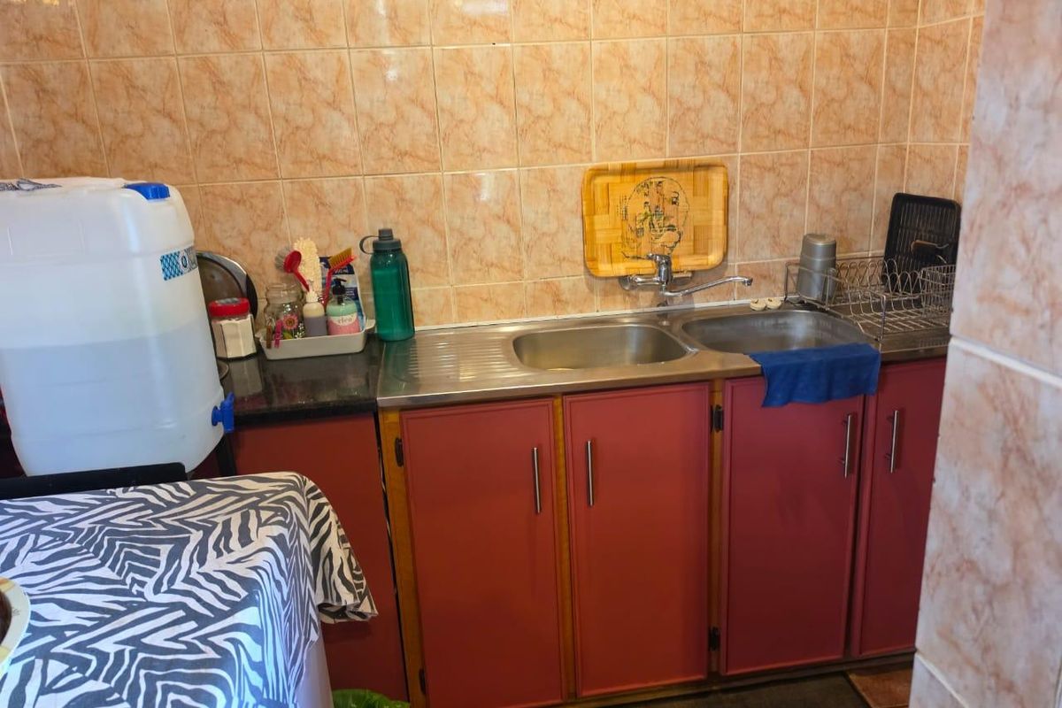A compact kitchen area featuring a double stainless steel sink, built-in cabinetry, and tiled wall finishes.
