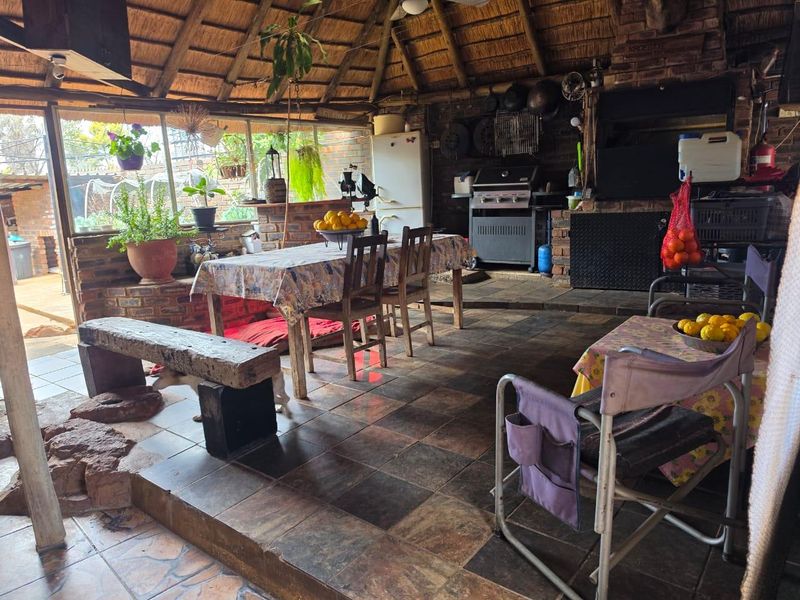 A rustic covered patio featuring a thatched roof, exposed brick walls, and a built-in braai area, perfect for outdoor entertaining.