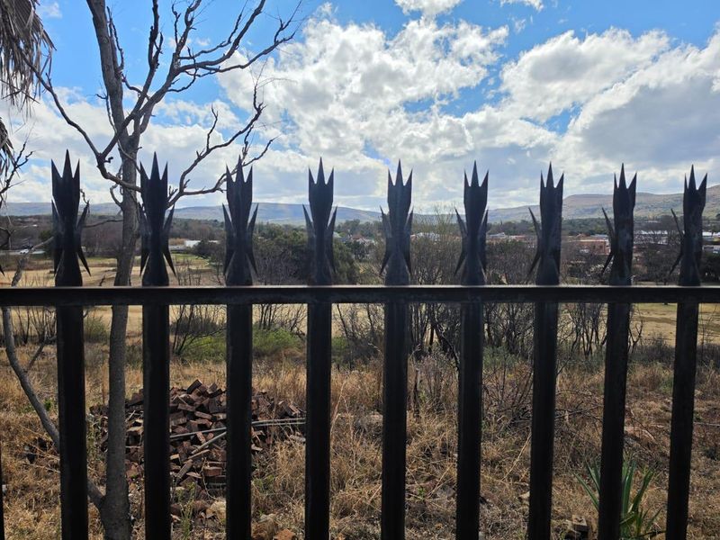 A view of the surrounding landscape and hills captured through a metal security fence with spiked toppers.