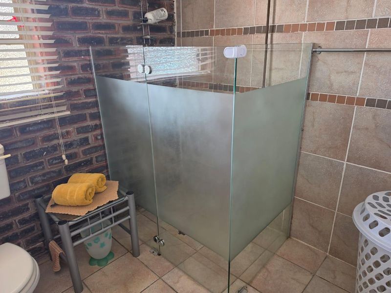 Bathroom featuring a glass shower enclosure, exposed brick wall accents, and neutral ceramic tiling throughout.
