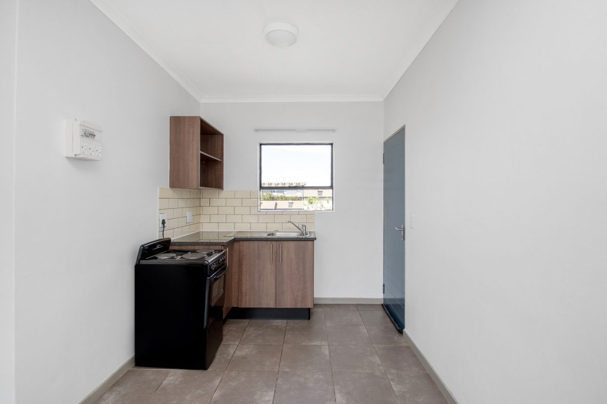 A compact, functional kitchen featuring wood-finish cabinetry, tiled backsplash, dark countertops, and tiled flooring, providing a clean and practical cooking space.