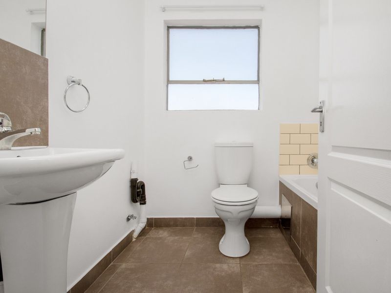 A functional bathroom featuring a pedestal basin, toilet, and bathtub with tiled splashbacks and flooring. The space is clean but shows exposed plumbing.