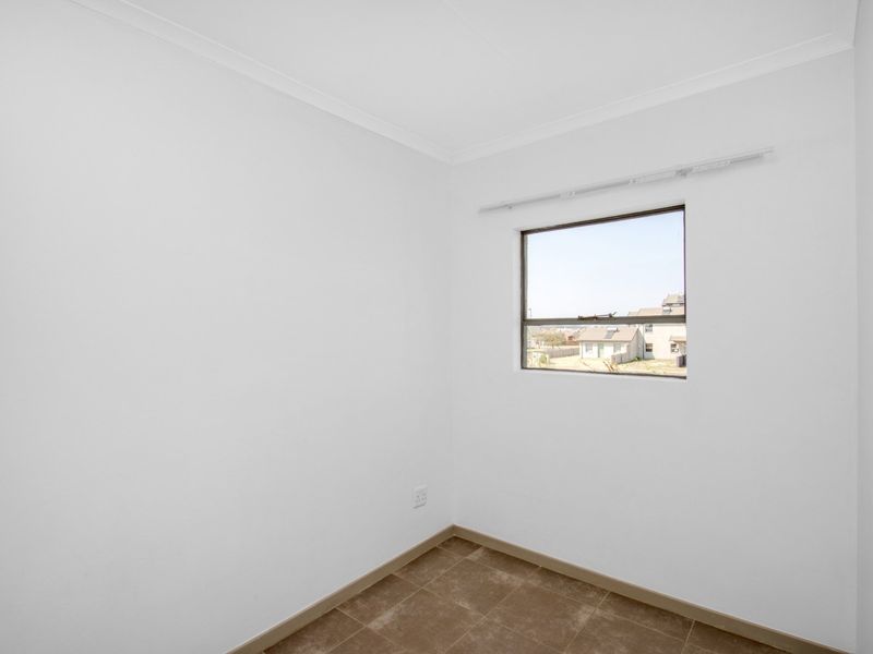 A clean, empty bedroom featuring neutral tiled flooring, white walls, and a window with a curtain rod installed.