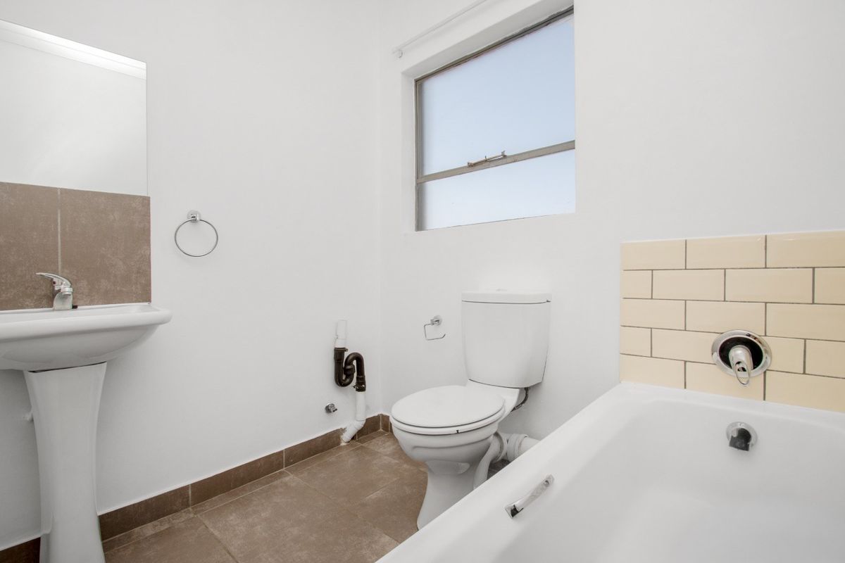 A functional bathroom featuring a pedestal basin, standard toilet, and bathtub with tiled splashback, finished with neutral floor tiles.