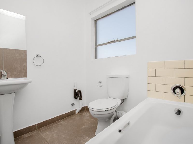 A functional bathroom featuring a pedestal basin, standard toilet, and bathtub with tiled splashback, finished with neutral floor tiles.