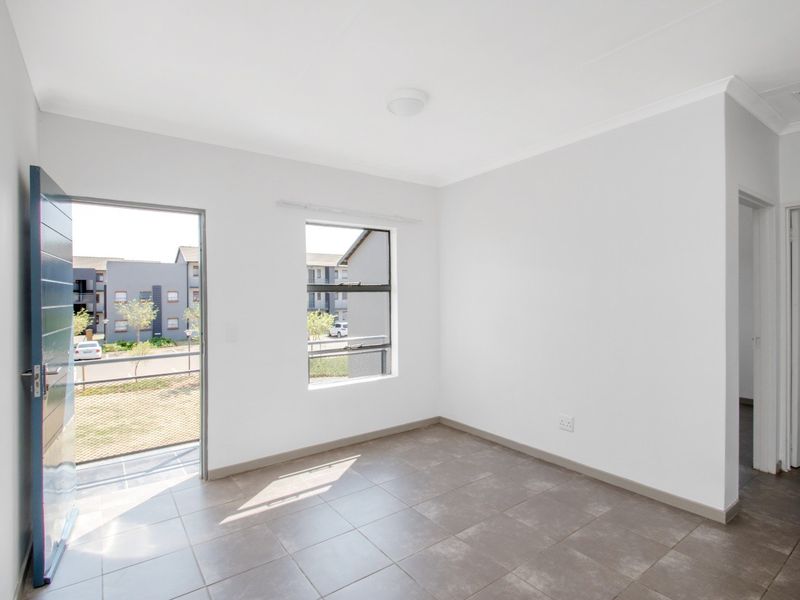 A bright, empty living area featuring neutral tiled flooring, clean white walls, and direct access to an outdoor balcony space.