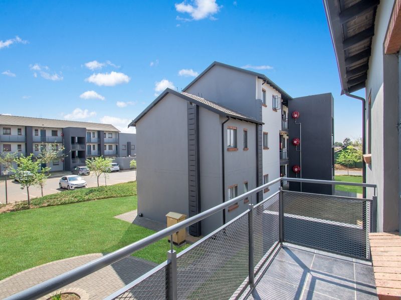A private balcony with tiled flooring and metal mesh railing, overlooking the apartment complex grounds and parking area.