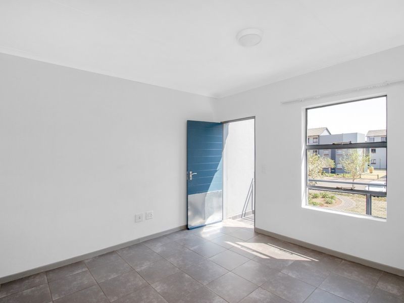 A bright, empty bedroom featuring neutral tiled flooring, clean white walls, and a door leading to an outdoor balcony area.