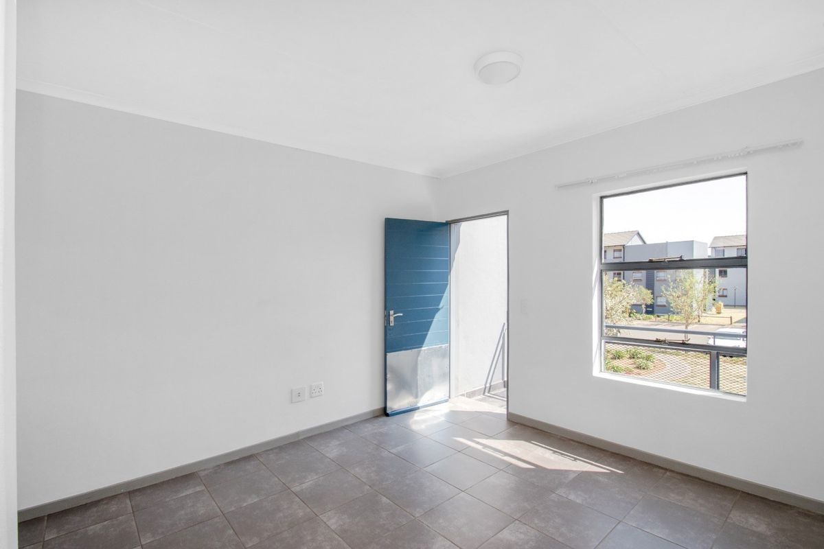 A bright, empty bedroom featuring neutral tiled flooring, clean white walls, and a door leading to an outdoor balcony area.