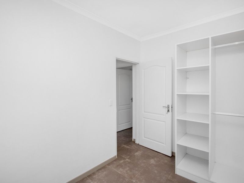 A clean, empty bedroom featuring neutral tiled flooring, white walls, and a built-in wardrobe with shelving and hanging space.