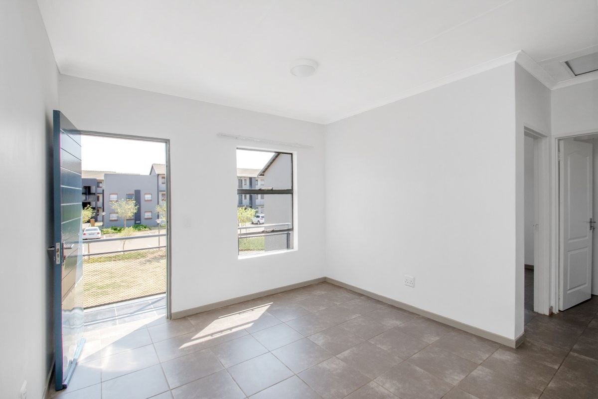 A bright, empty living area featuring neutral tiled flooring, clean white walls, and direct access to an outdoor balcony space.