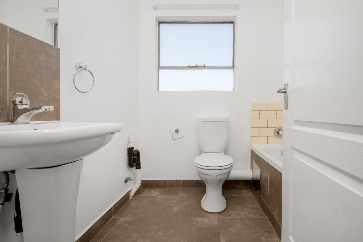 A functional bathroom featuring a pedestal basin, toilet, and bathtub with tiled splashbacks and flooring. The space is clean but shows exposed plumbing.
