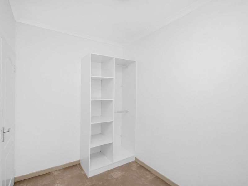 A clean, empty bedroom featuring tiled flooring and a built-in white wardrobe with shelving and hanging space.
