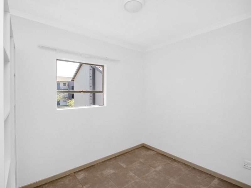 A clean, empty bedroom featuring neutral tiled flooring, built-in shelving, and a window providing natural light.