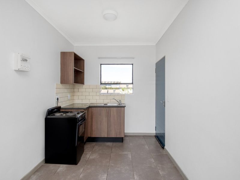 A compact, functional kitchen featuring wood-finish cabinetry, tiled backsplash, dark countertops, and tiled flooring, providing a clean and practical cooking space.