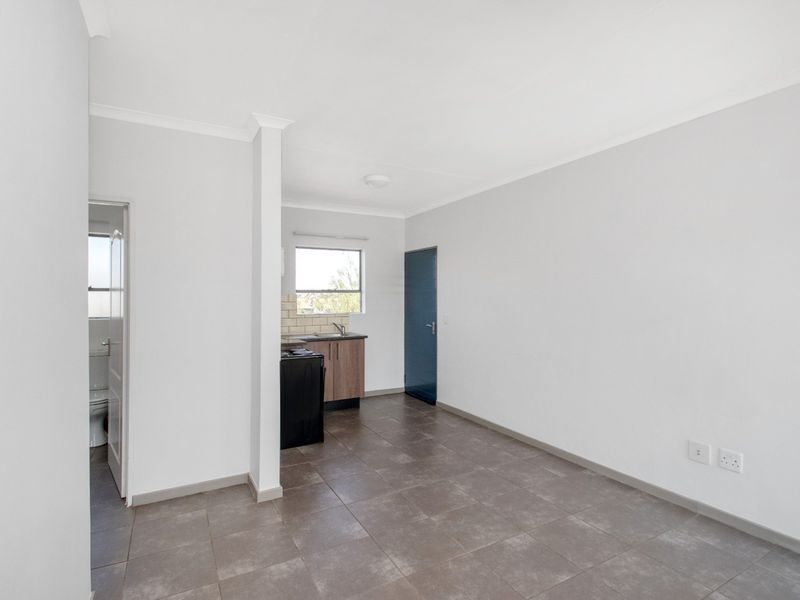 An open-plan living area featuring tiled flooring, a compact kitchen with built-in cabinetry, and access to an adjacent bathroom.